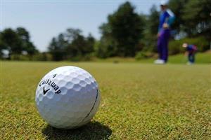 Close-up of a golf ball on the green with golfers in the background.